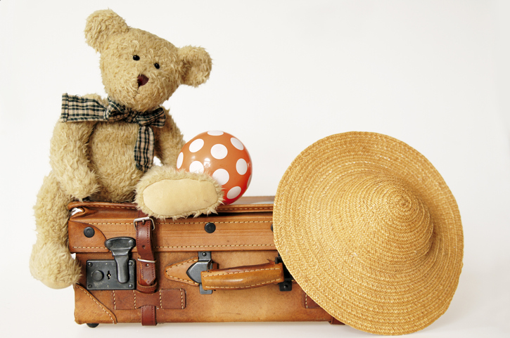 Teddy bear on suit case with hat and ball